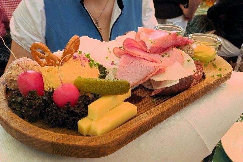 platter of cheese, ham, radishes, pickles on a wooden platter